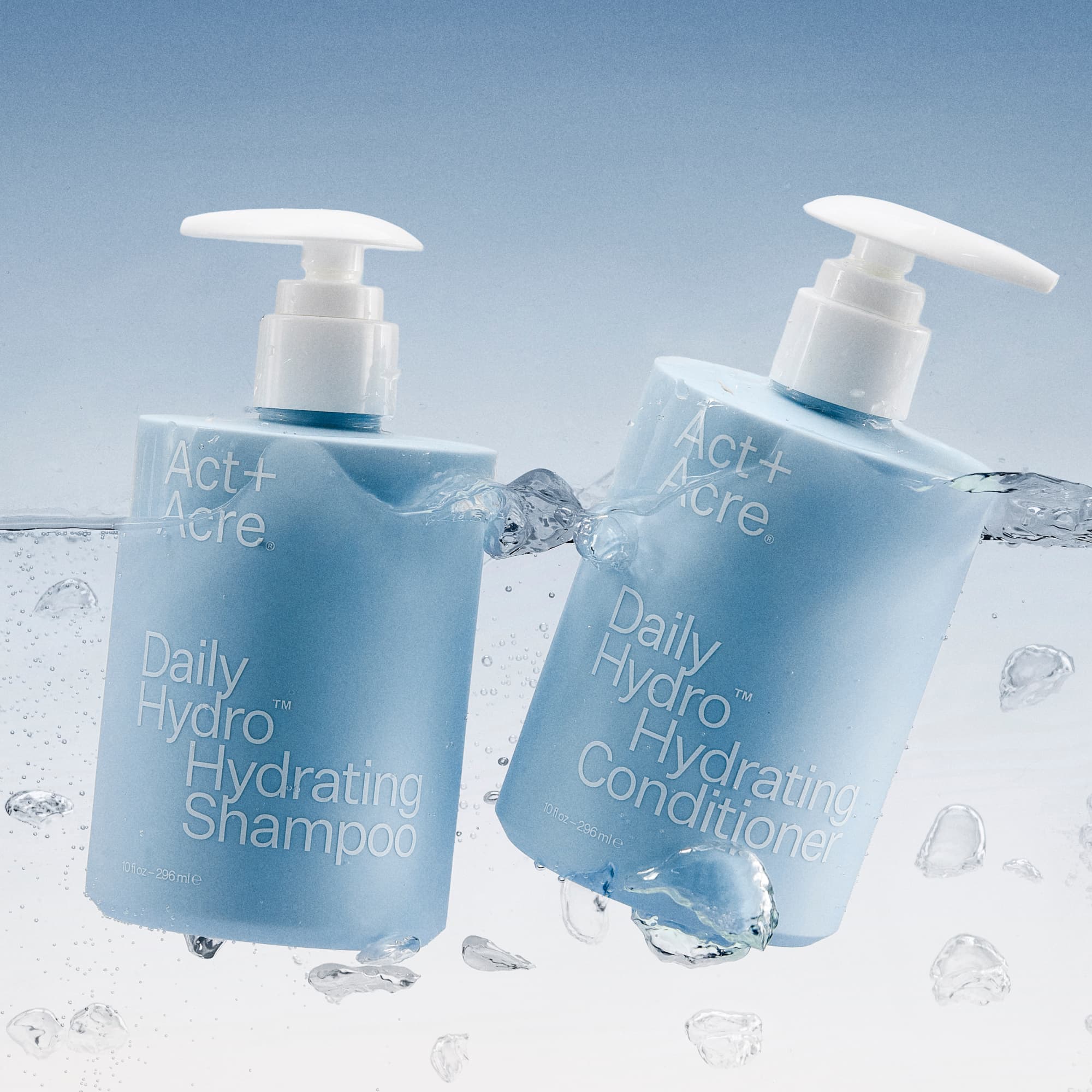 Two bottles of Act+Acre Daily Hydro™ Hydrating Shampoo and Conditioner with water droplets on a light blue background.